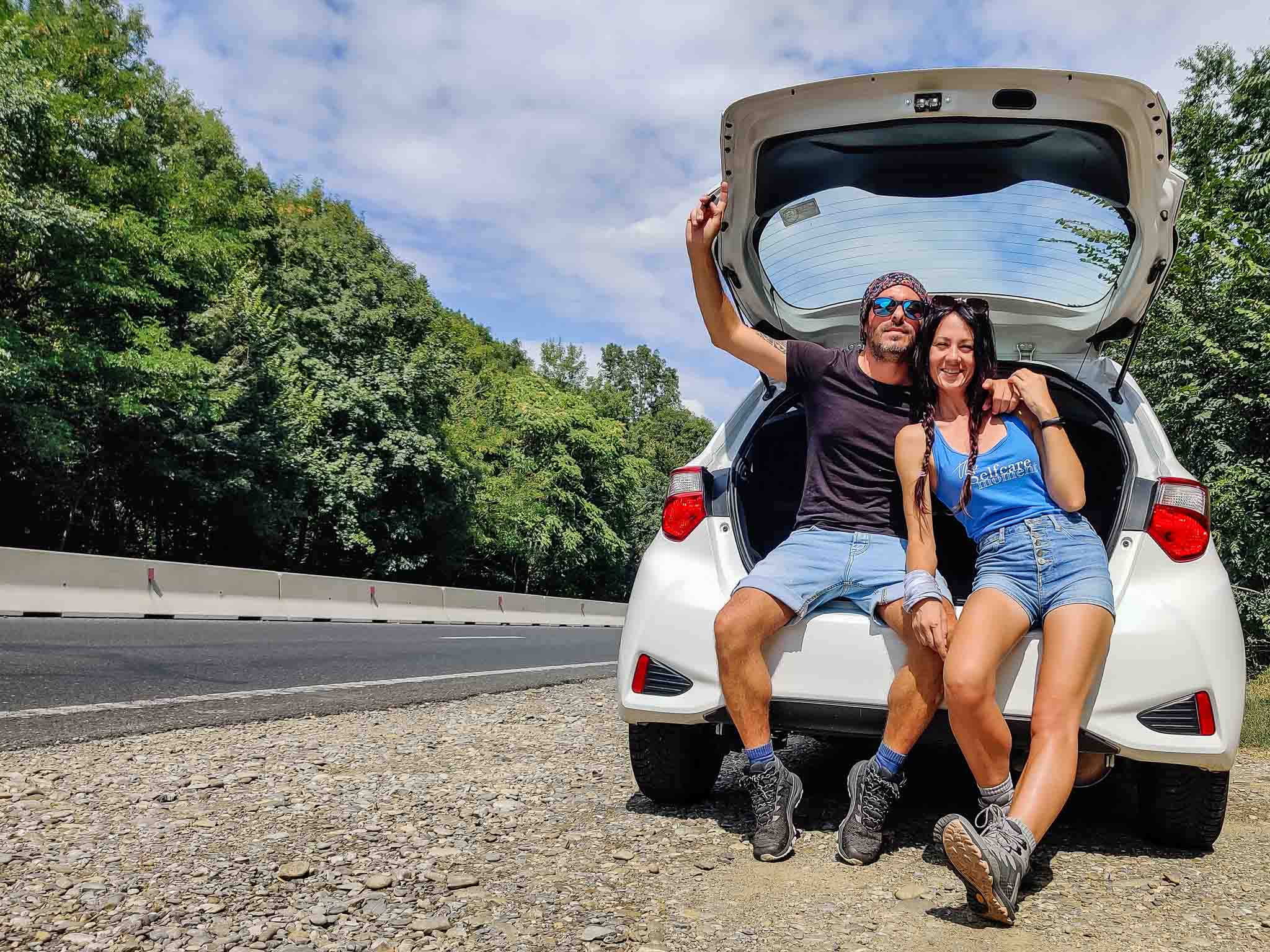 A couple sitting on the boot of a car on the side of the road